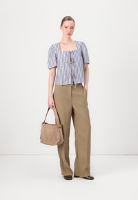 Blouse bleu clair et blanche à rayures avec des manches bouffi, avec un décolleté lacé, associée à un pantalon beige taille haute et un sac à main beige doux.