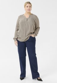 Blusa de rayas en tono topo claro con escote en V y detalle de botones, combinada con jeans de mezclilla de pierna ancha en azul oscuro y zapatos negros de punta.