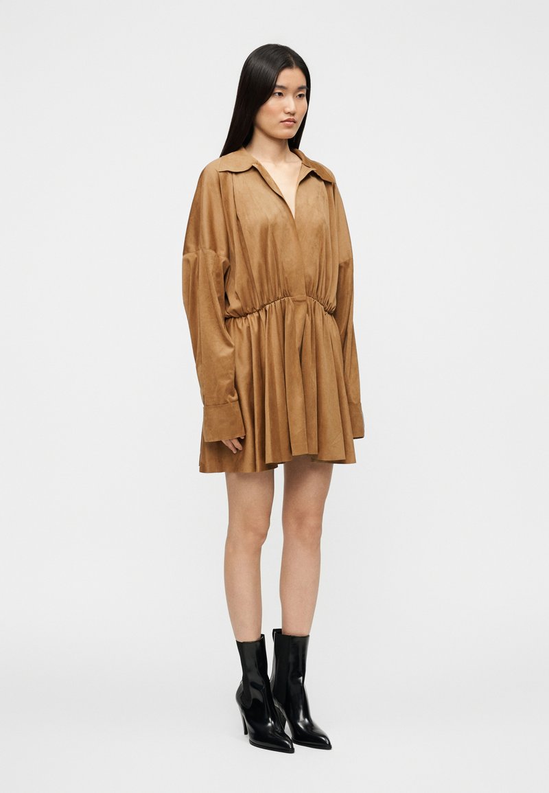 Braunes Wildlederkleid mit Kragen, langen Ärmeln, tailliertem Bund und ausgestelltem Rock. Kombiniert mit schwarzen, hochhackigen Stiefeletten.