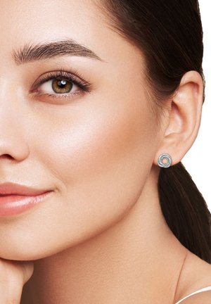 Boucles d'oreilles en argent avec un design en spirale, présentant une texture métallique lisse et une forme arrondie, portées dans le lobe de l'oreille d'un modèle.