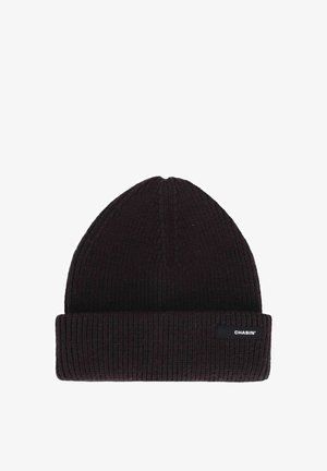 Tumšs adīts cepures beanie ar ribotu tekstūru un salocītu maliņu. Malā ir taisnstūra melns uzlīme ar baltu tekstu.