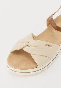 Beige plátěné sandály s uzlovým designem vpředu, vycpanou tanovou stélkou a hnědým páskem. Obsahují bílou gumovou podrážku s akcentem zlatého loga.