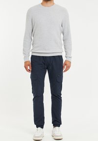 Pull gris côtelé associé à un pantalon cargo bleu marine avec poches et fermetures éclair, complété par des baskets blanches. Tenue décontractée et pratique.