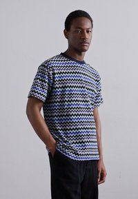 Lühikeste varrukatega must särk, millel on sinise ja rohelise tooni nöörmuster. Sile tekstuur ja ümmargune kaelus.