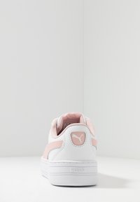 Biały but sportowy z różowymi akcentami, z górą z gładkiej skóry, teksturowanym obcasem i gumową podeszwą. Logo Puma na tabliczce pięty.