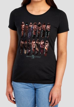 Woman wearing black Mortal Kombat t-shirt with character faces and names, paired with light blue jeans.