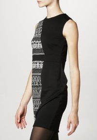 Robe noire à la silhouette ajustée, présentant un panneau blanc à motifs d'un côté et une texture lisse de l'autre. Encolure ronde, sans manches.