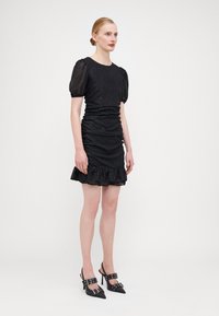 Robe noire à sequins avec des manches courtes bouffantes, un ourlet volanté et une silhouette ajustée. Associée à des chaussures à talons hauts noires avec des accents de boucle.