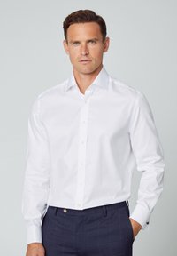 Witte button-up shirt met een klassieke kraag, lange mouwen en standaard manchetten; gladde stof; gecombineerd met donkerblauwe geruite broek.