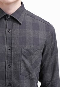 Camicia a quadri scura con bottoni, dotata di taschino sul petto, realizzata in tessuto leggero, con una finitura testurizzata e motivi sottili grigi e neri.