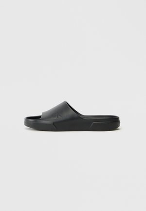 Black slide sandal made of smooth rubber with an open toe and a raised logo on the strap. Features a thick sole with a slight curve.