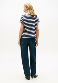 Top de rayas azul marino y blanco de manga corta combinado con pantalones anchos de mezclilla oscura y botas negras de tacón. Tejido de punto texturizado.