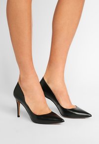 Černé kožené lodičky na vysokém podpatku s špičatou špičkou a elegantní siluetou. Podpatky jsou štíhlé, což podtrhuje elegantní design.