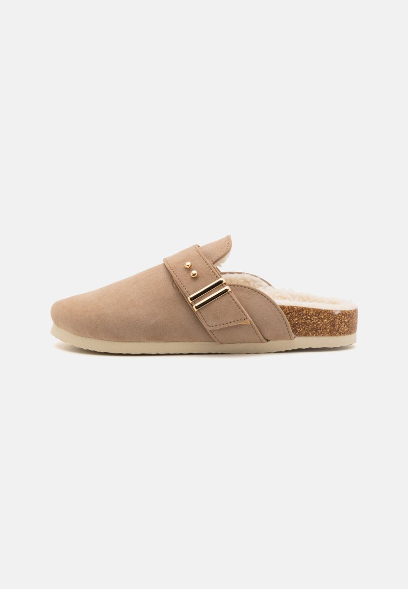 Ανοιχτό καφέ σουέντ παντοφλέ με υφή στο εσωτερικό, πλευρική ζώνη και χρυσές διακοσμητικές αγκράφες, διαθέτει σόλα τύπου φελλού για στήριξη.