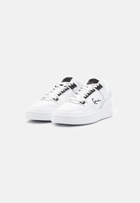 White sneakers with black accents, made of smooth leather. Features include laces, a cushioned sole, and a logo on the side.