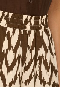 Bruine en crèmekleurige rok met een elastische tailleband. De stof heeft een zachte textuur en bevat een golvend, abstract patroon.