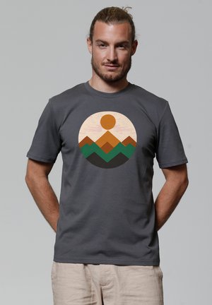 Grijze katoenen t-shirt met een circulaire grafiek van een gestileerde zon boven meerkleurige bergen in tinten bruin en groen.