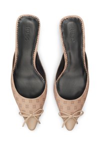 Μπεζ mules που φοριούνται εύκολα, με υφή στο πάνω μέρος και σχέδιο με λογότυπα, μυτερή μύτη και φιόγκο μπροστά. Μαύρα πέλματα στο εσωτερικό.