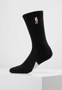 Juodas sportinis kojinės su garbanotu tekstūru, NBA logas viršutinėje pusėje, baltos akcentai ant pirštų ir kulno, vidutinio ilgio.