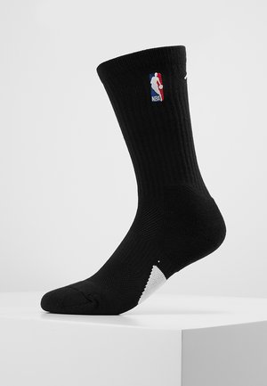 Calzino sportivo nero con texture a coste, logo NBA sul lato superiore, dettagli bianchi sulla punta e sul tallone, di lunghezza media.