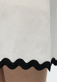 Άσπρο ύφασμα με μαύρη κυματιστή περίμετρο πάνω σε γυμνό δέρμα, που δείχνει υφή και αντίθεση μεταξύ των υλικών.