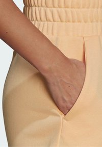 Persikofärgad tyg med en slät textur, med ett elastiskt midjeband och en sidoficka där en hand är insatt.