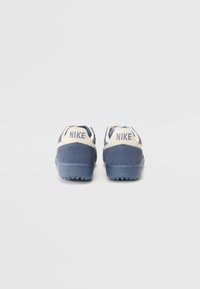 Baskets Nike bleu et crème en matériaux de suède et de cuir, semelle texturée et logo "NIKE" au talon. Design classique à profil bas.