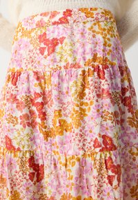 Jupe à volants fleurie en tissu léger, ornée de fleurs roses, rouges et oranges sur un fond crème, avec des détails froncés aux coutures.