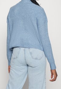 Ljusblå stickad tröja med rundad halsringning, sänkta axlar och cropped nederkant, kombinerad med ljusblå högmidjade jeans.