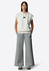 Kermanit pääntie ilman hihoja, jossa on musta logo, yhdistettynä leveälahkeisiin harmaisiin collegehousuihin. Molemmat on valmistettu pehmeästä, teksturoidusta kankaasta.