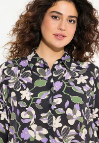 Blusa nera floreale con fiori viola e verdi, chiusura frontale con bottoni, colletto, tessuto testurizzato, con accenti scritti a mano sul motivo.