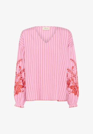 Roosa pluus vertikaalsete valgete triipudega, V-kaelus ja pikad varrukad. Omab detailset punast lilleline tikandit varrukatel ja kogutud mansettidel.