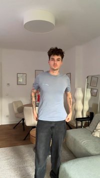 Ανοιχτού μπλε βαμβακερό μπλουζάκι με στρογγυλή λαιμόκοψη και κοντά μανίκια, με ένα μικρό λευκό λογότυπο στο αριστερό στήθος. Φορεμένο με μαύρα τζιν.