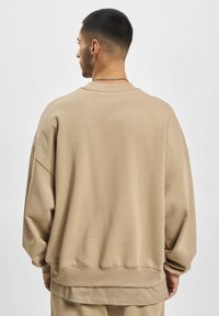 Beige oversized sweatshirt with ribbed cuffs and hem, made of soft fabric. Features a crew neck and dropped shoulders for an relaxed fit.
