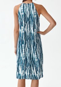 Vista trasera de un vestido halter hasta la rodilla con un patrón abstracto en azul y blanco, tejido ligero y ajuste holgado.