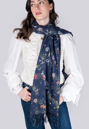 Navy scarf featuring floral and animal patterns, made of soft fabric with fringed edges, worn over a textured white blouse.