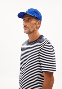 Cappellino di cotone blu con visiera curva e logo ricamato, indossato con una maglietta a maniche corte a righe blu e bianche. Vista di profilo laterale.