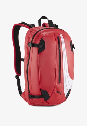 Mochila Puma roja con tirantes acolchados, bolsillo frontal con cremallera vertical, detalles en negro, diseño curvo blanco y correas de compresión laterales.