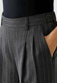 Pantalons en chevron gris avec de subtils rayures, présentant une taille ajustée, des plis à l'avant et des poches latérales.