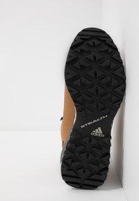 Chaussure de sport marron et grise avec une semelle en caoutchouc noire présentant un motif de bande de roulement texturé. Comprend les inscriptions « STEALTH » et « adidas ».