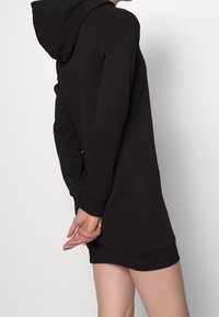 Sudadera negra con capucha, fabricada con tela suave, con mangas largas y un ajuste estándar, con dobladillo redondeado y puños ajustados.