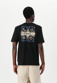 Black cotton t-shirt featuring a colorful graphic print on the back, including sun and crescent moon motifs, and a tag at the hem.