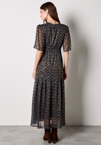 Długa, granatowa sukienka z teksturowanym wzorem nachodzących na siebie łuków w kolorze złotym, różowym i zielonym. Krótkie rękawy, wcięcie w talii oraz warstwowa spódnica.