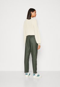 Cremefarvet ribbestrikket sweater med ballonærmer, parret med olivengrønne tapered bukser og hvide sneakers med teal-accenter, set fra ryggen.
