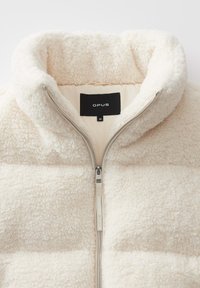 Giacca di pile bianca con colletto alto, design trapuntato, zip metallica e un'etichetta interna che mostra il marchio "OPUS" e la taglia 36.