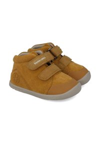 Zapatos altos de ante marrón con dos correas de Velcro, suelas de goma y un detalle de logo circular en el costado. Interior forrado suave.