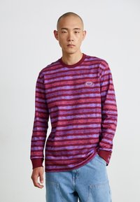 Long-sleeve shirt in maroon and purple with horizontal stripes, featuring a crew neck and ribbed cuffs, with a logo on the chest.