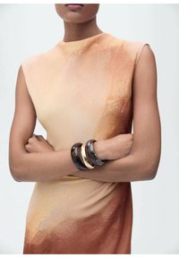 Oranje en beige verloop jurk met een hoge halslijn. Drie gestapelde armbanden: een zwarte, een gemarmerde en een met gouden accent. Gladde textuur.