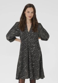 Schwarzes Kleid mit V-Ausschnitt und kurzen Puffärmeln, das ein Wellenmuster in Weiß und Gold aufweist. A-Linien-Silhouette, knielanges Design.