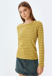 Langärmliges gelb-weiß gestreiftes Shirt mit Rundhalsausschnitt, kombiniert mit einem Jeansrock. Der Stoff wirkt strukturiert und lässig.